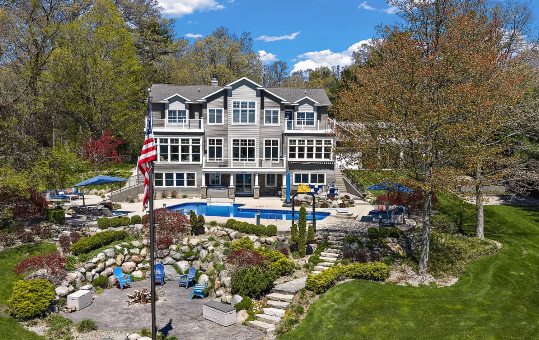 Aerial view of the estate at 15074 Mercury Drive: a three-story lakefront house above a pool, terraced gardens, and lawn